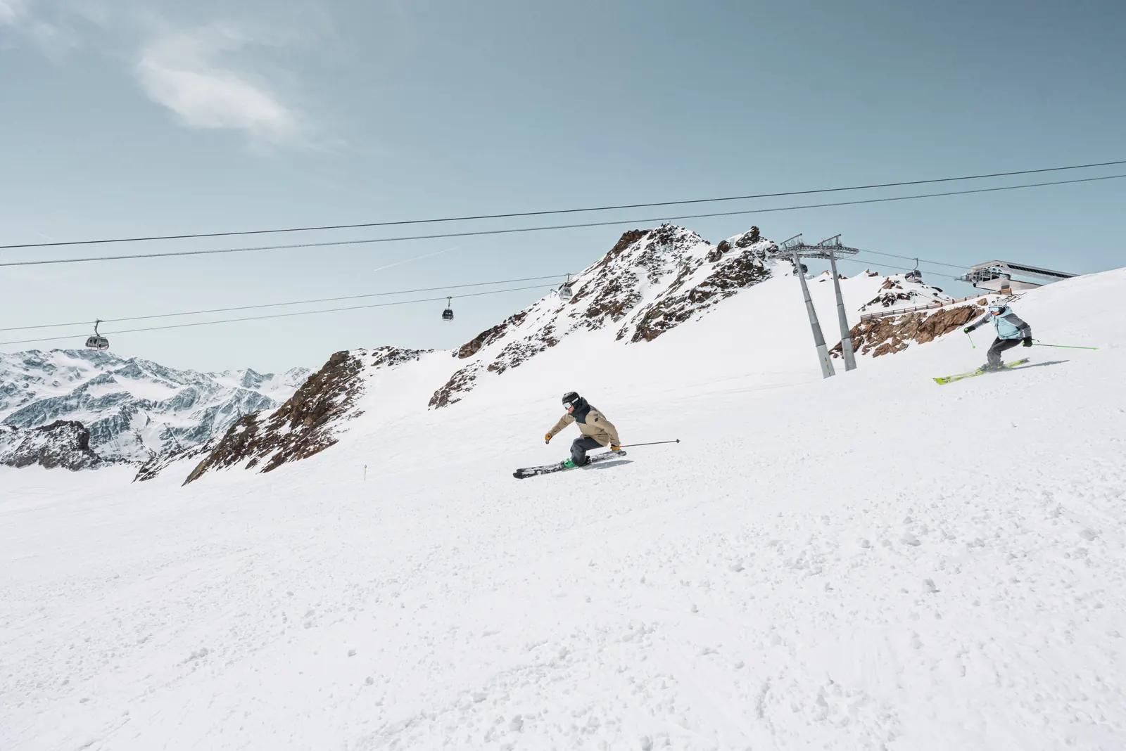 Zwei Skifahrer auf der Gletscherpiste am Rettenbachferner in Sölden, darüber eine Gondelbahn