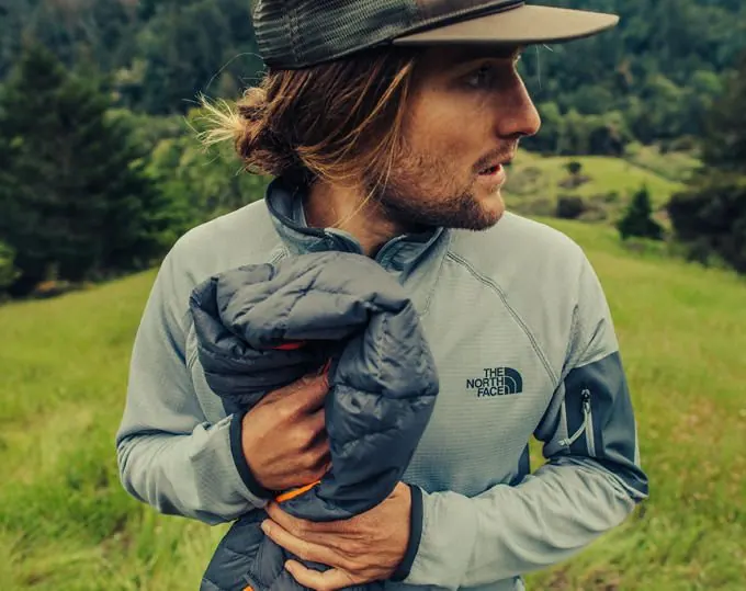Mann in The North Face Fleecejacke hält eine zusammengerollte Daunenjacke, vorhandenes Shopmotiv