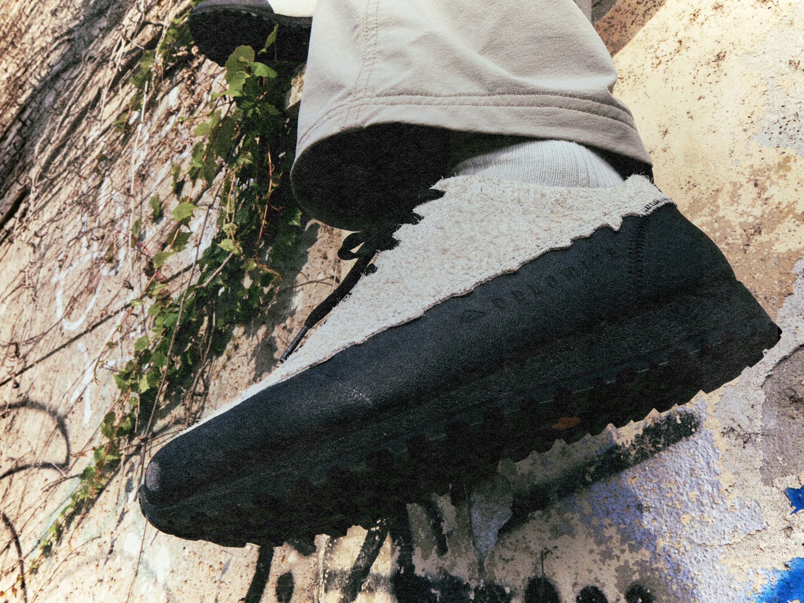 Nahaufnahme der Vibram-Sohle eines Dolomite-Schuhs mit grobem Profil, im Hintergrund Efeu und eine besprayte Betonwand
