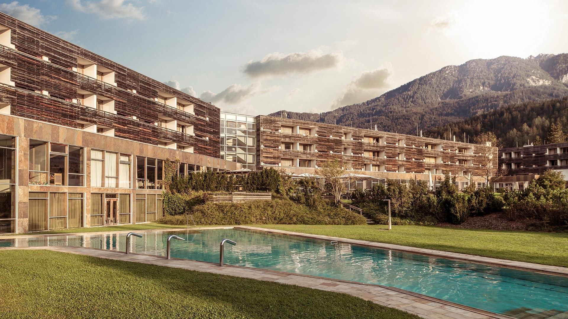 Außenpool und Hotelfassade des Falkensteiner Carinzia in Tröpolach vor einem bewaldeten Berghang