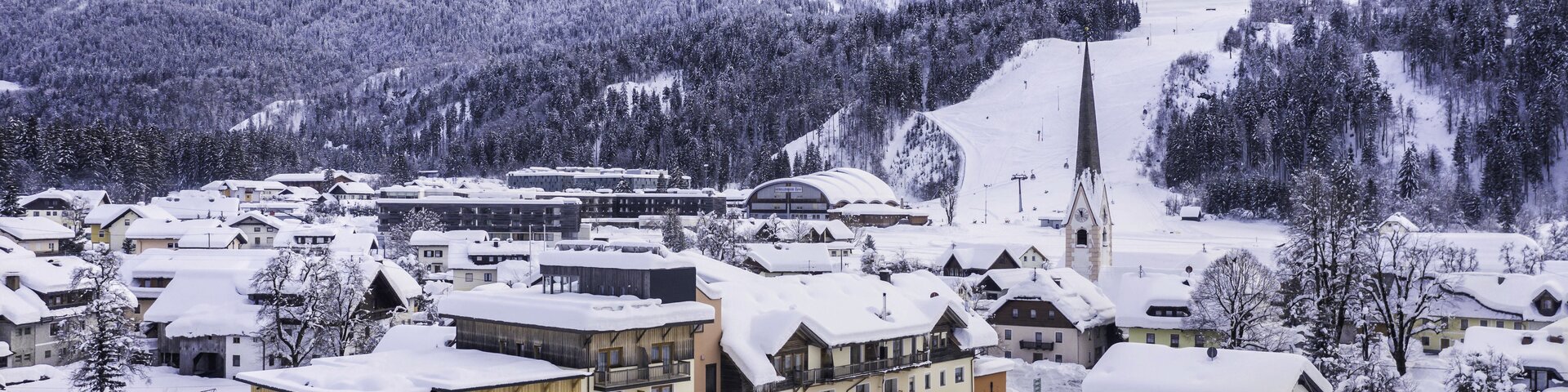Hotel Samerhof und verschneite Häuser in Tröpolach mit Skipiste im Hintergrund