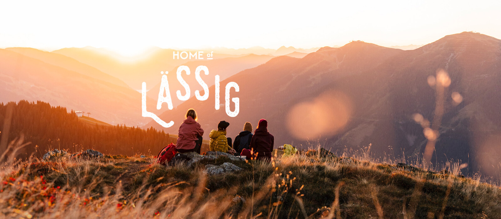 Vier Wandernde im Abendlicht über Saalbach Hinterglemm mit dem Schriftzug Home of Lässig